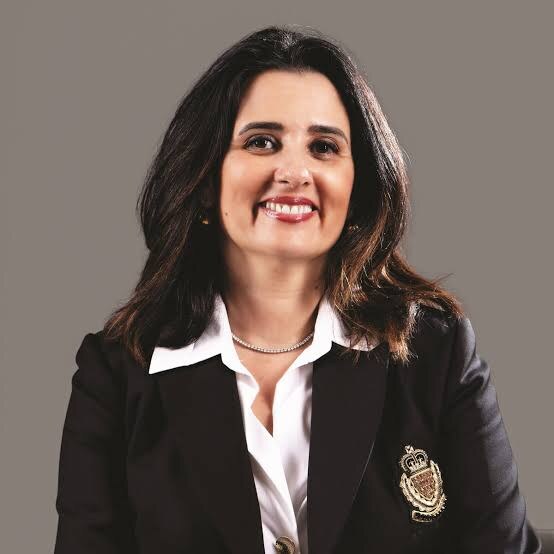 Formal portrait of Lamia Tazi wearing a dark blazer against a neutral grey background